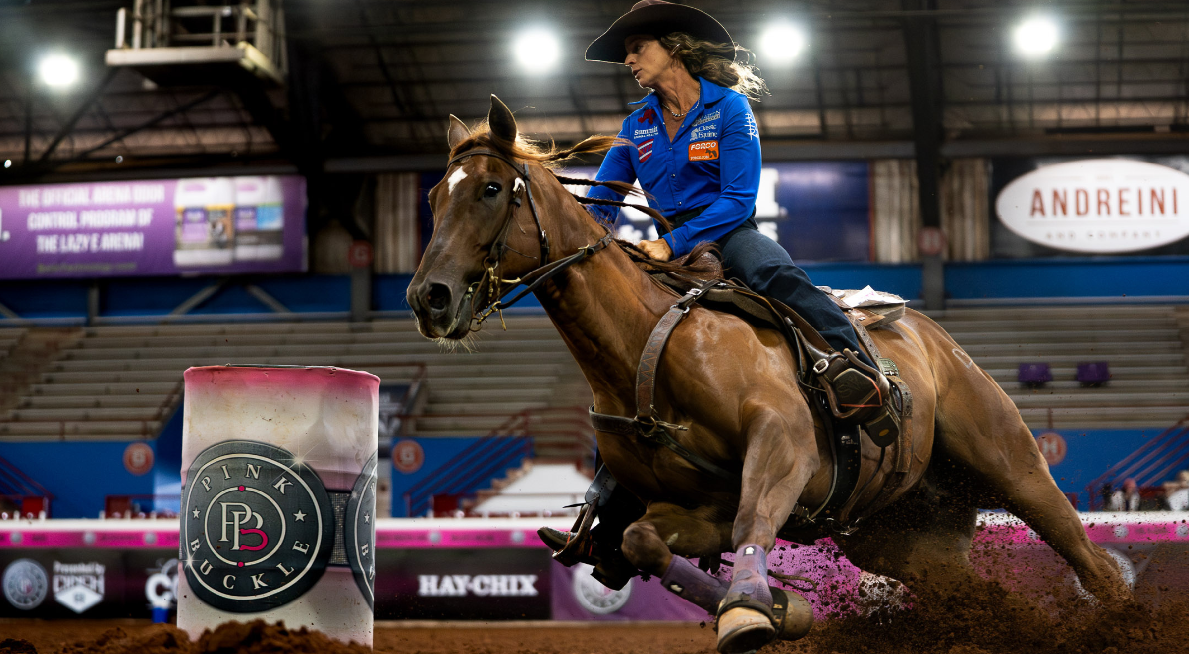 Close view of Martin Saddlery leather reins held taut as the horse rounds a pink-and-white barrel mid-run.
