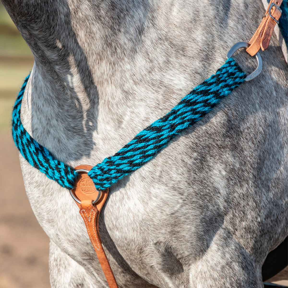 Turquoise-black mohair breastcollar on a gray horse, seen at the chest. The 2-inch mohair strands join a tan leather center piece with a ring, and one side runs up to a ring and tug strap at the saddle.