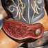Chestnut Alpine spur strap with flower tooling worn on a cowboy boot, seen up close. The tooled flower and leaves fill the strap inside white stitching.