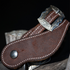 Chocolate roughout spur strap seen up close on a spur, against a dark background. White stitching follows the edge of the roughout leather up to the engraved Prescott buckle.