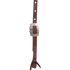 Prescott buckle on a chocolate roughout headstall cheek, seen up close. Engraving covers the scalloped buckle frame, and a latigo bit tie knots through the strap end below.