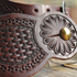 Chocolate Tombstone spur strap seen up close on a wood rail. A stamped flower surrounds the spur button beside the basket tooled center and San Carlos border.
