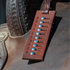 Leather cow counter resting on a saddle seat, hung from the saddle horn. Numbered slots hold metal rivets that slide to track which cows have been called in team penning and ranch sorting.