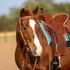Sorrel horse with a white blaze wearing a harness leather browband headstall, standing saddled in an arena. The headstall's Prescott buckle sits on the cheek above the bit.