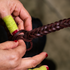 Hands braiding chocolate latigo strands into a roping rein, seen up close in the workshop. The finished 5 plait braid runs off to one side.