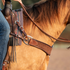 Martin Saddlery chocolate steer roper breastcollar on a buckskin horse, seen at the shoulder with a rider in the saddle. The quilted strap ends in a smooth leather tab at a ring, with buckled tug straps running to the saddle.