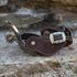 Chocolate roughout cowboy spur straps with Prescott buckles on a pair of spurs resting on a rock ledge. White stitching edges the straps, and the engraved buckle faces forward.
