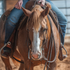 Sorrel horse with a blaze seen head on, ridden in heavy latigo split reins that hang down both sides of the neck. The rider holds the dark reins above the saddle horn in an arena.