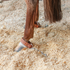 Horse's hind leg in stall shavings wearing a Martin Saddlery kick chain. A leather strap buckles around the pastern, with a short chain trailing from its ring.