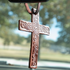 Tooled leather cross air freshener hanging from a rearview mirror, with trees and a field blurred behind. Scroll tooling covers the brown leather cross.
