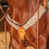 Natural alpaca and mohair breast collar on a horse, seen from the front at the chest. The wide band of natural fiber strands meets a tan leather center piece with a round maker's stamp, with a tie-down strap below.