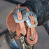 Natural harness leather spur straps with Salinas buckles hanging from a saddle horn, seen up close. The engraved buckles sit side by side above an engraved spur.