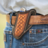 Mini weave angled knife scabbard worn on a leather belt with jeans, holding a folding knife. A natural basketweave panel sits inside chocolate leather with white stitching.