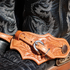 Natural oak leaf spur strap with acorn oak tooling buckled over a black cowboy boot, seen up close. White stitching follows the leaf shaped edge around the tooled leather.