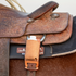 Tooled saddle on a sorrel horse with a natural roughout rope powder holder hanging from the back D-ring. A white powder bottle sits in the pocket above the cinch strap.