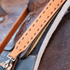Rope can strap in natural roughout seen up close against a tooled saddle. Chocolate buckstitching runs down both sides of the strap inside white stitching, ending at a swivel snap.