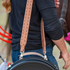 Person carrying a rope can over one shoulder by a natural roughout buckstitched strap. Snaps join the strap to the can's handle, with a saddled horse behind.