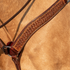 Weathered antique breast collar strap lying against a buckskin horse's shoulder, seen up close. The weave stamp fills the center of the skirting leather strap inside dark edges with white stitching.