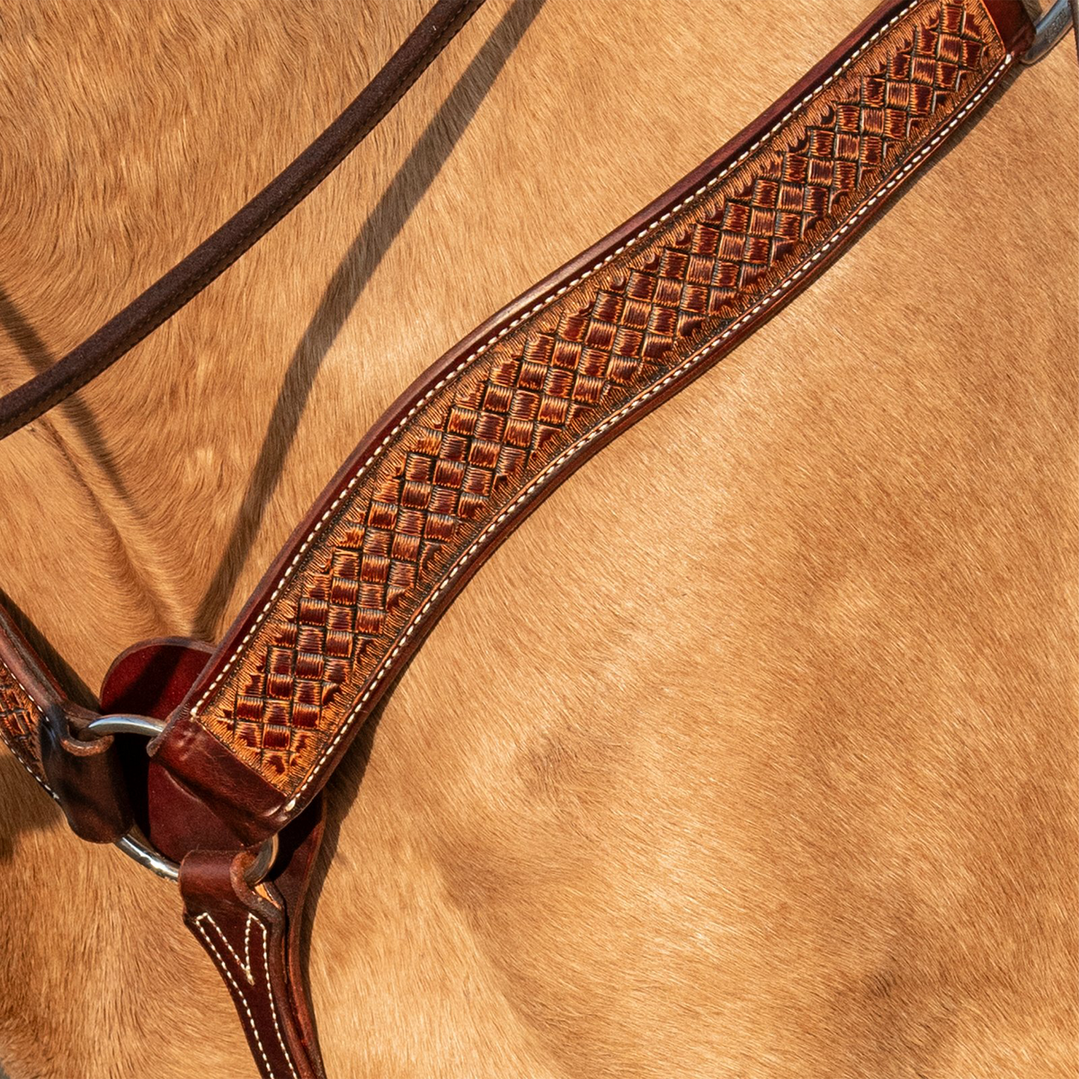 Weathered antique breast collar strap lying against a buckskin horse's shoulder, seen up close. The weave stamp fills the center of the skirting leather strap inside dark edges with white stitching.