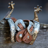 Pair of engraved spurs hooked over a weathered fence rail with natural harness spur straps attached. The stitched straps hang between the spur shanks with the engraved buckles facing out.