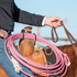 Rider on a sorrel horse holding braided reins, with a pink rope hung from the saddle by a bungee rope strap. The bungee loops over the coils at the swell.