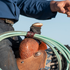 Rider in a blue shirt reaching forward beside a saddle horn where a latigo rope strap holds a green rope. The leather strap loops around the coils above the tooled swell.
