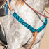 Western breast collar in turquoise-black mohair on a gray horse, seen at the shoulder. The mohair strap runs from a ring at the saddle down to a leather center piece on the chest.