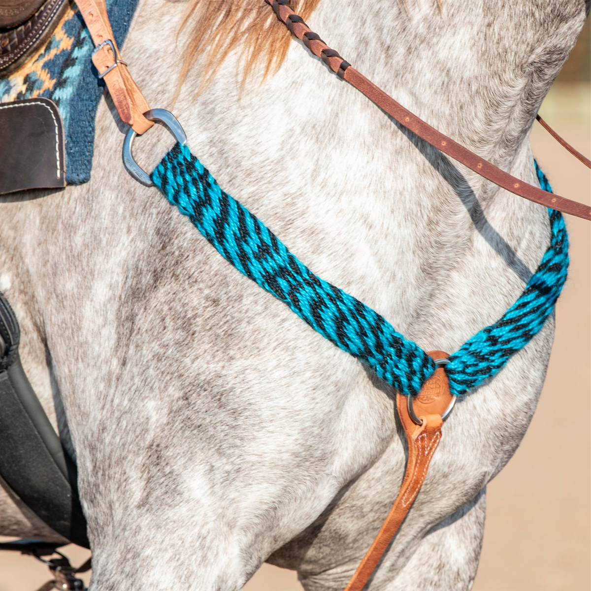 Western breast collar in turquoise-black mohair on a gray horse, seen at the shoulder. The mohair strap runs from a ring at the saddle down to a leather center piece on the chest.