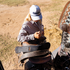 A woman in a white rope cap seen from above as she works on a saddle outdoors. The dark embroidered logo and braided bill rope are visible on the cap.