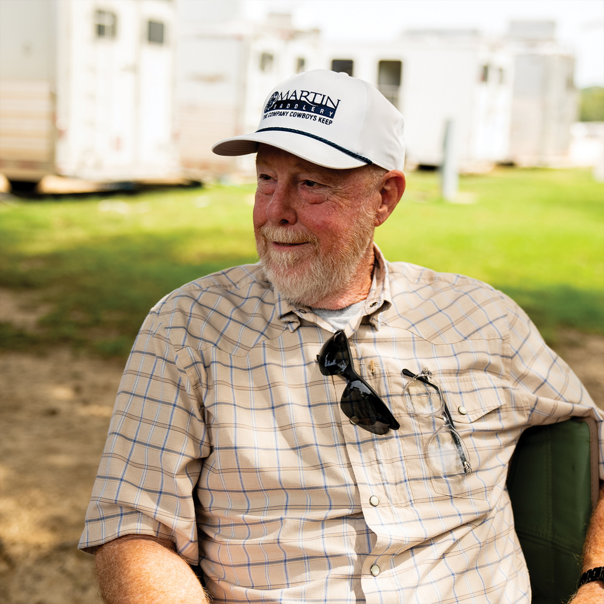 A man with a white beard wearing a white five panel rope cap, seated outdoors and smiling. The cap has a dark Martin Saddlery logo and a rope across the bill.